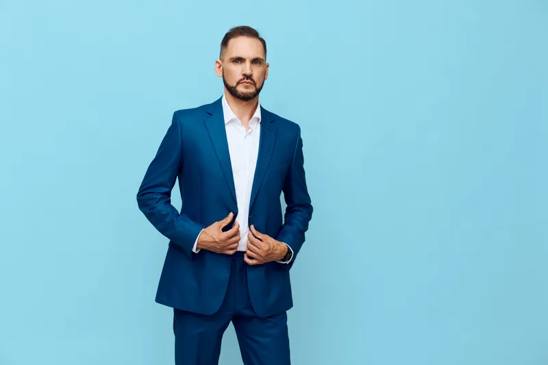 A professional man in a tailored blue suit stands against a solid color backdrop, projecting confidence, focus, and readiness for business challenges.