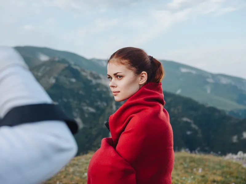 Женщина-путешественница с красным пледом на плечах в горах
