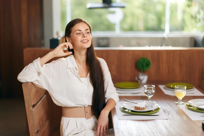 Счастливая женщина наслаждается романтическим ужином дома с вкусным блюдом на обеденном столе