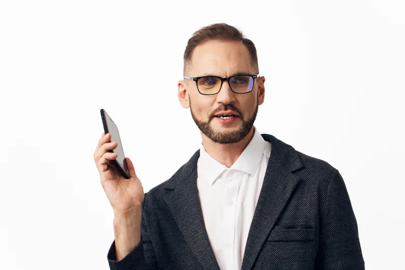 Professional man in a blazer holds a phone, exuding confident emotion. Isolated solid colored background highlights business focus, leadership aura, and professional presence in business media.