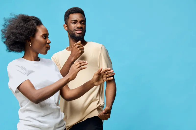 A joyful African couple dancing together against a vibrant blue background, expressing happiness and connection through their lively movements and casual attire