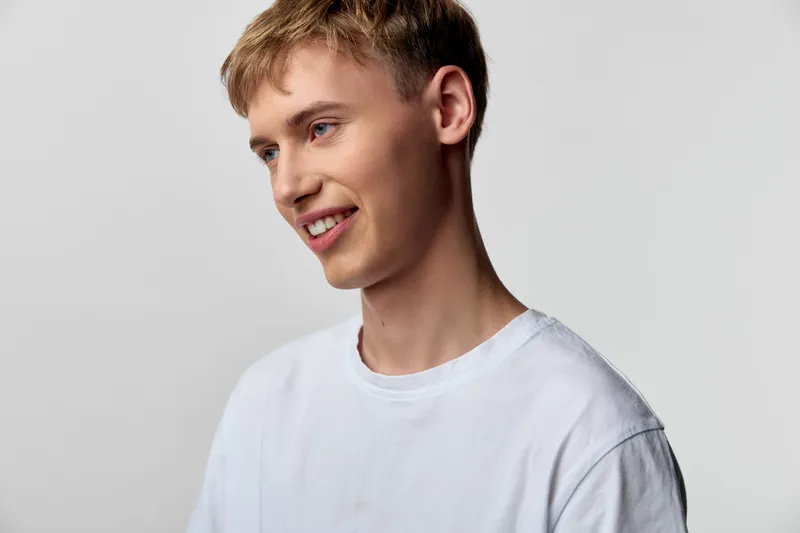 Young male with a cheerful smile wearing a white tee in a studio setting, casual and relaxed pose, soft lighting highlighting a friendly mood and confident appearance