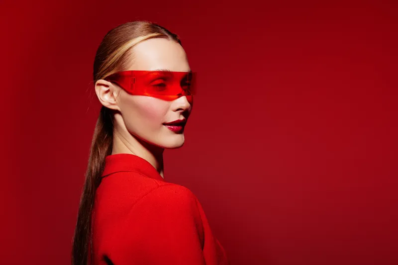 Portrait of a stylish woman wearing red sunglasses and a red outfit against a red background. Concept of fashion, modern style, and bold color contrast in studio lighting.