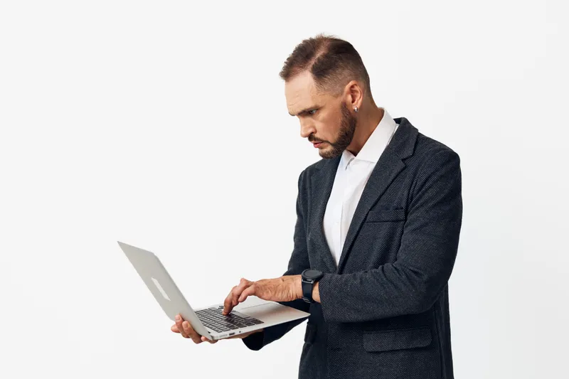 A business professional man stands with a laptop, presenting calm focus and confident determination on an isolated colored background. The scene emphasizes professional mood, poised posture, and