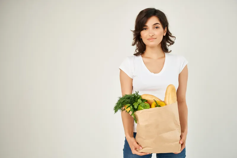 Весёлая брюнетка в белой футболке доставляет пакет с продуктами