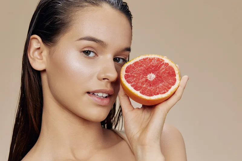 Женщина с грейпфрутом в руках улыбается на изолированном фоне