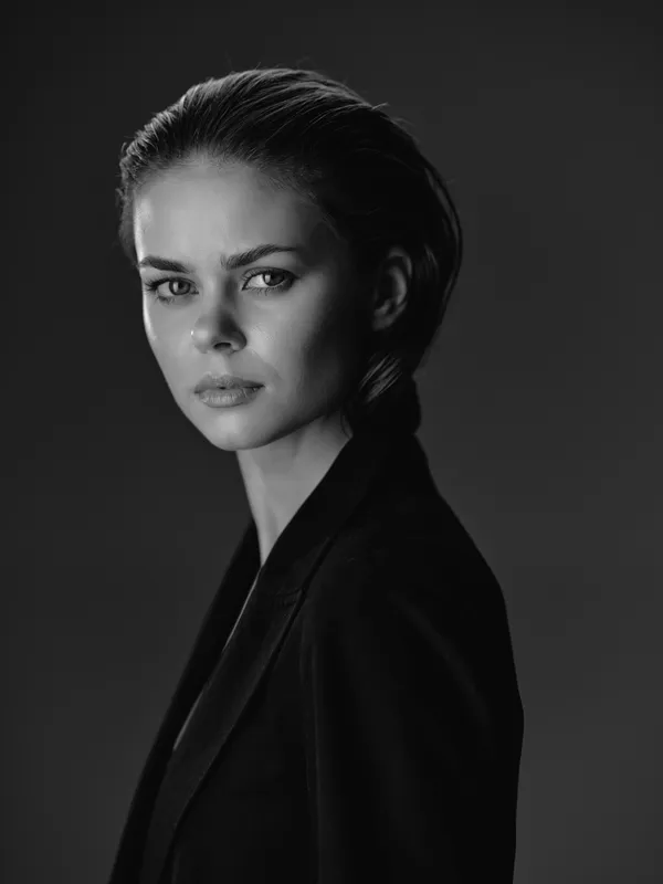 Black and white portrait of a serious woman with short hair wearing a dark jacket in a studio setting.