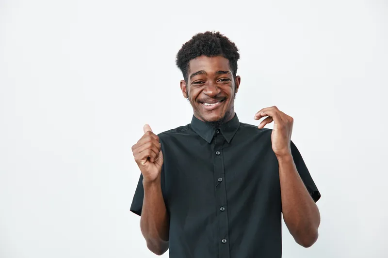 Young African American man with dark skin smiling and wearing black shirt on white background. Portrait of happy male with curly hair expressing joy and confidence.