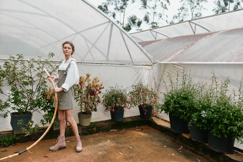 Young woman watering plants in a greenhouse, dressed in a casual outfit, displaying joy and connection with nature, vibrant greenery around her, perfect for eco friendly themes
