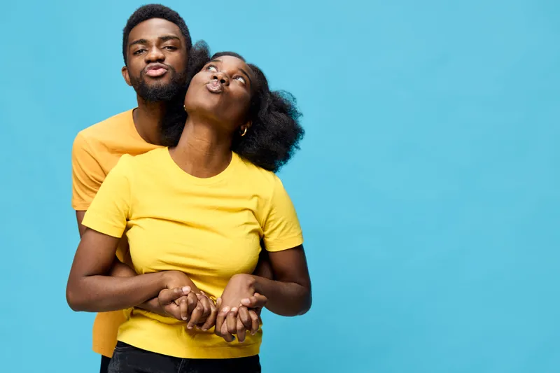 Happy young couple playfully posing together in colorful outfits for a joyful portrait, showcasing love and affection on a vibrant blue background