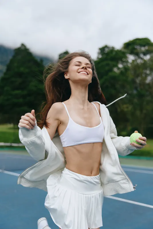 Joyful young woman playing tennis outdoors in sporty attire, showcasing health and vitality against a lush green background