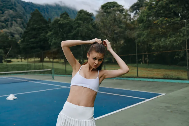 Young athlete adjusting her hair on the tennis court, showcasing determination and style in activewear, highlighting fitness and sports lifestyle