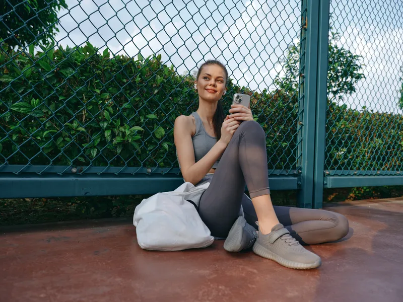 Спортивная девушка отдыхает на земле со смартфоном в руках