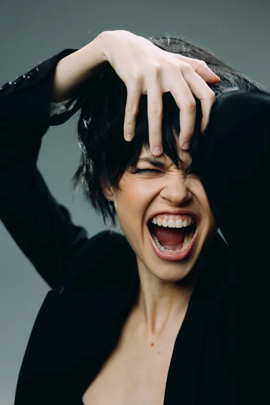 expressive woman screaming with hand in hair, dramatic emotion, dark outfit, intense mood