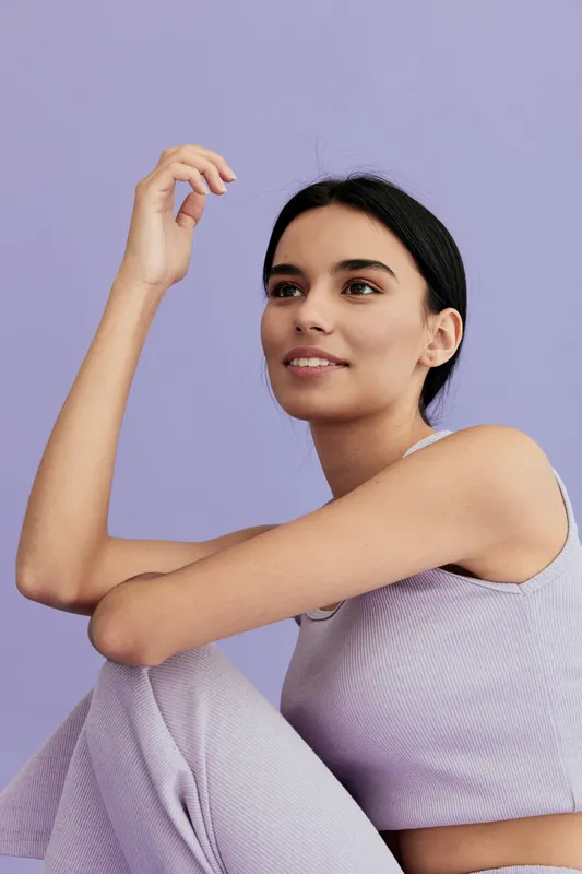 young woman with dark hair in lilac outfit posing thoughtfully against lavender background, showing relaxed and calm expression, casual summer style