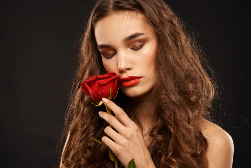 Женщина с красной розой на темном фоне, длинные волосы, макияж, красные губы