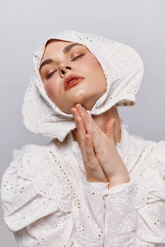 Serene young woman in white dress and bonnet, expressing tranquility and humility, perfect for seasonal themes and fashion concepts