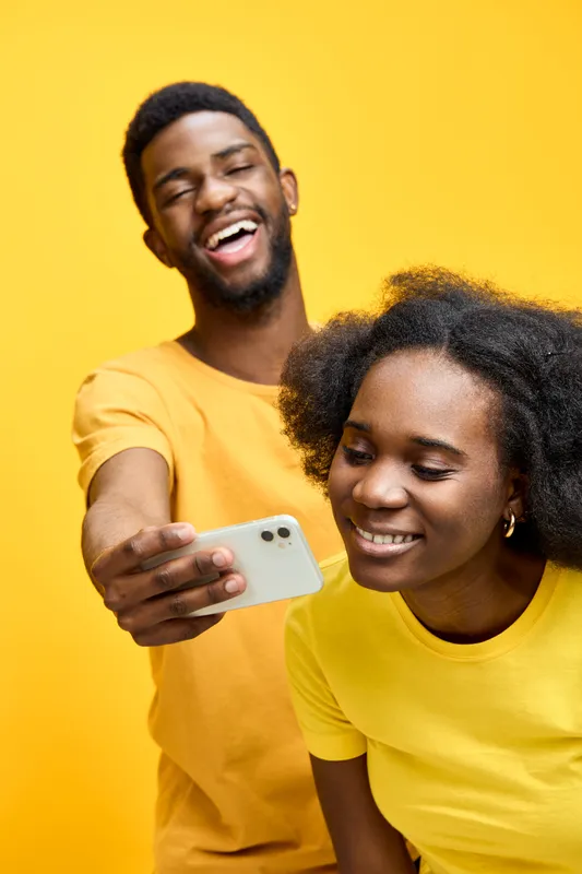 Happy young African couple enjoying a moment together while taking a selfie against a vibrant yellow background, showcasing joy and connection