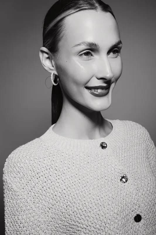 Portrait of a smiling white woman with fair skin wearing hoop earrings and a knit sweater with buttons, studio black and white photo.
