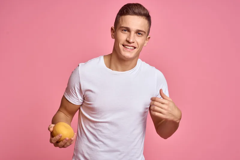Мужчина с фруктами в руках на розовом фоне