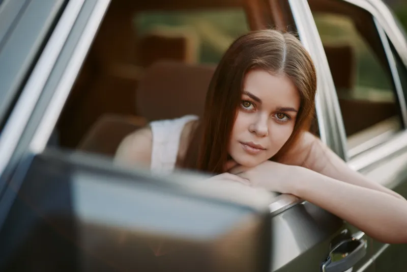 Young woman relaxing in a car with a serene expression, bathed in soft natural light during the golden hour, evoking feelings of freedom and adventure.