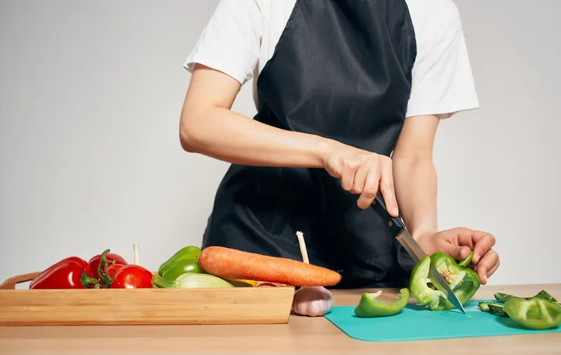 Приготовление здоровой пищи на кухне, черный фартук, нарезка овощей