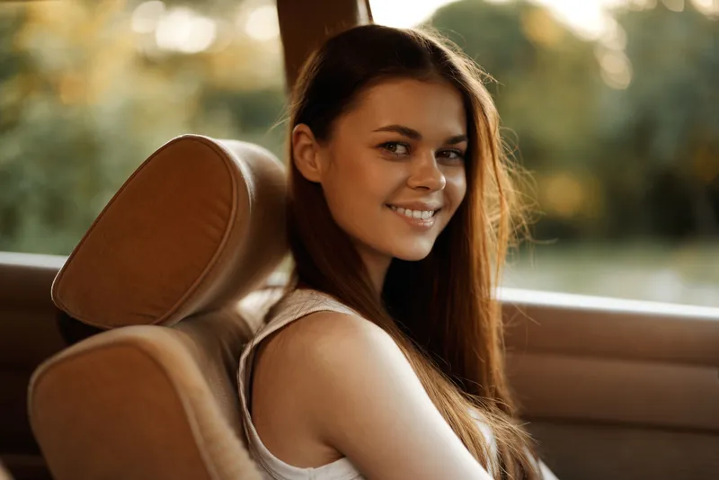 Smiling young woman with long hair in a car, enjoying a sunny day, conveying happiness and freedom.