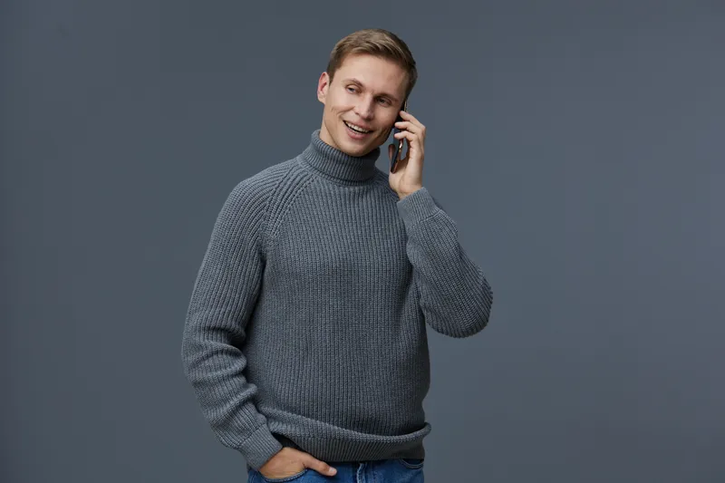 Smiling young man wear grey turtleneck sweater use mobile phone for video call digital nomad concept isolated dark background