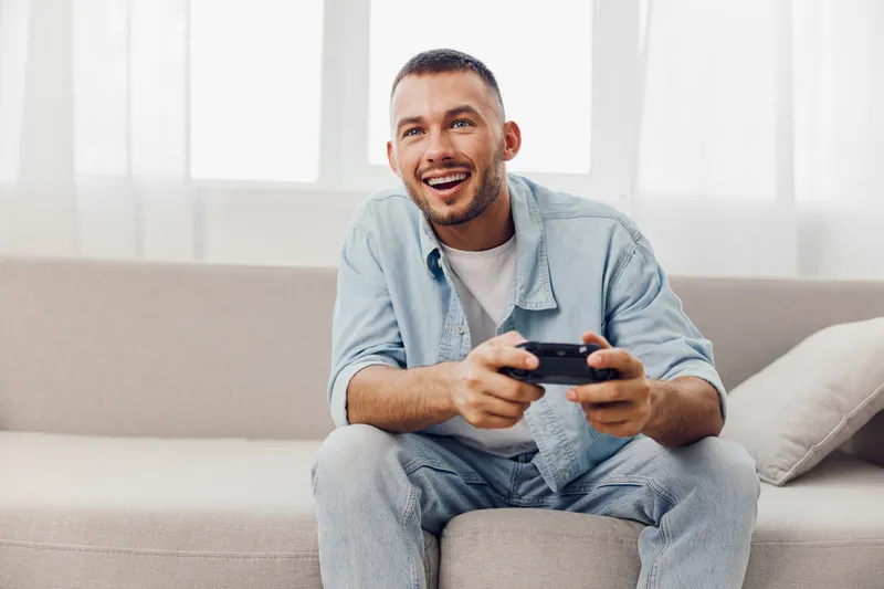 Happy man playing video games at home, enjoying his digital detox while embracing authentic imperfection and soft masculinity in a cozy atmosphere.