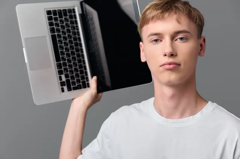 Casual scene of a male holding a laptop overhead, showcasing modern technology and portable device in a sleek studio setting with a neutral background and focused expression