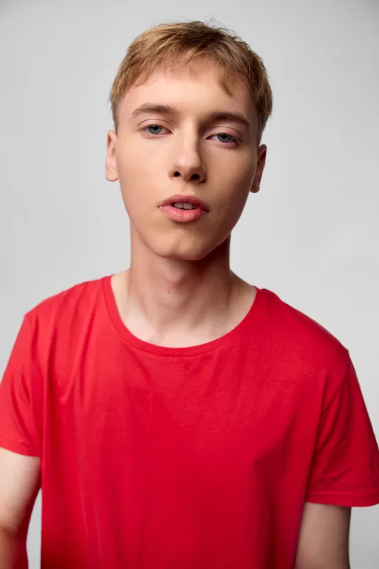 Young man in a red shirt looks at the camera with a casual expression, studio lighting and clean background for fashion, lifestyle or commercial use