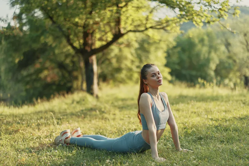 A young woman practicing yoga outdoors in a tranquil green setting, wearing a stylish blue outfit, showcasing peace and focus amidst nature s beauty