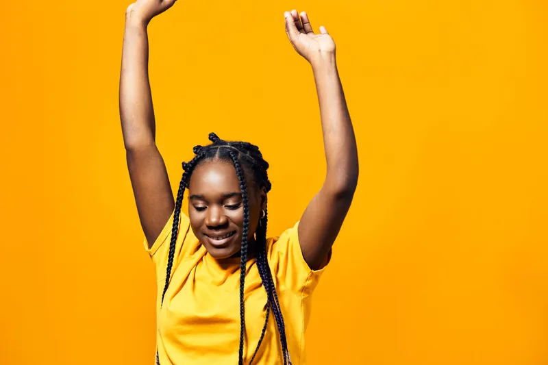 Happy girl with braids celebrating against a bright yellow background, wearing a cheerful yellow t shirt, conveying joy and positivity