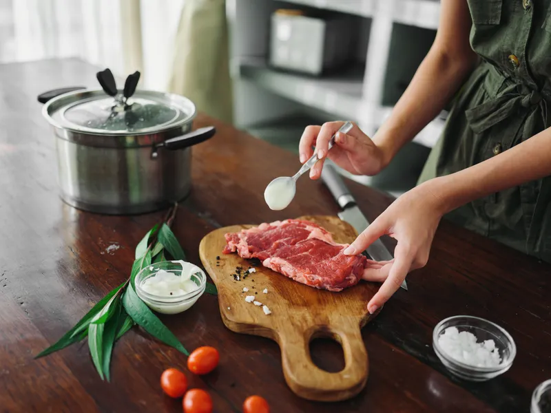 Женщина на кухне готовит ужин из мяса, овощей и специй на деревянном столе на фоне стильной кухни