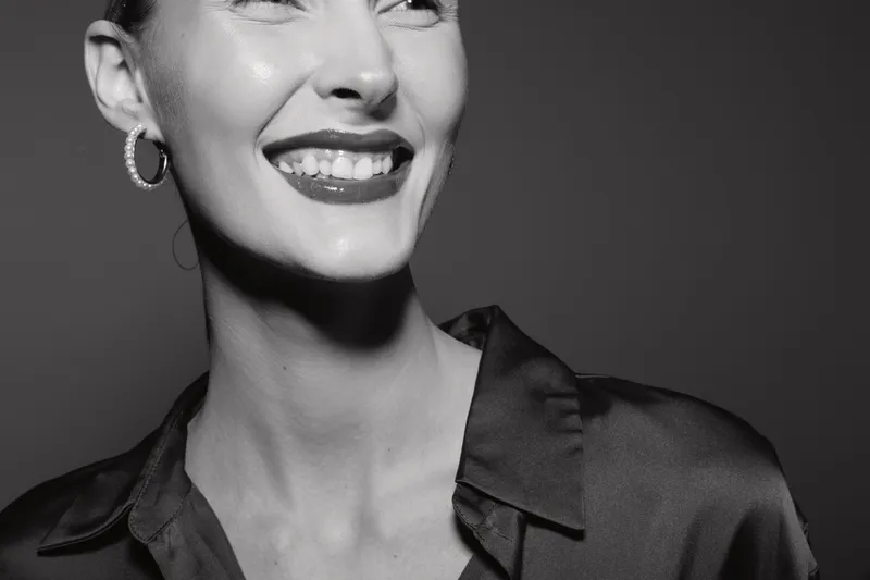 Close-up of a smiling Caucasian woman with fair skin in a dark silky blouse. The black and white portrait emphasizes happiness, elegance, and female beauty concept.