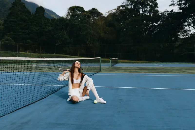 Happy young woman relaxing on a tennis court in white athletic attire, showcasing joy and tranquility in a serene outdoor setting