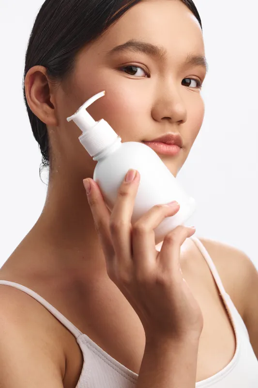 asian woman applies skincare product in a studio closeup, calm and confident, soft lighting highlights smooth skin and a healthy glow during a beauty routine.