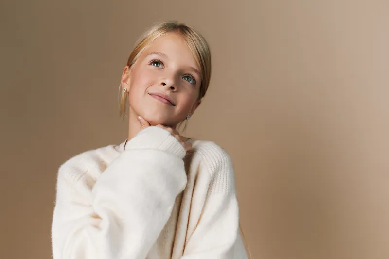 Portrait of a young woman wearing a plush cream sweater, soft lighting, and a gentle smile, conveying cozy fashion and natural beauty in a calm studio setting.