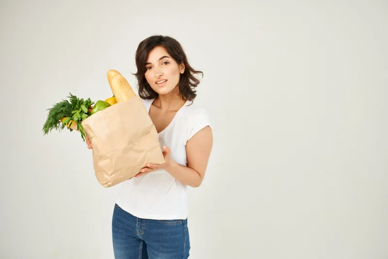 Женщина держит продукты, доставленные из супермаркета, на светлом фоне