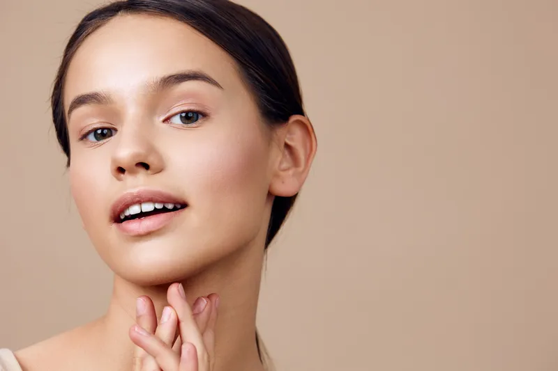 Beautiful young woman showcasing natural skincare with a soft smile, highlighting skin care products and healthy lifestyle in a minimalist background