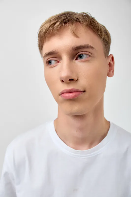 Young man looking away in a casual white t shirt under studio lighting, thoughtful expression and relaxed pose, head and shoulders composition for lifestyle or fashion use