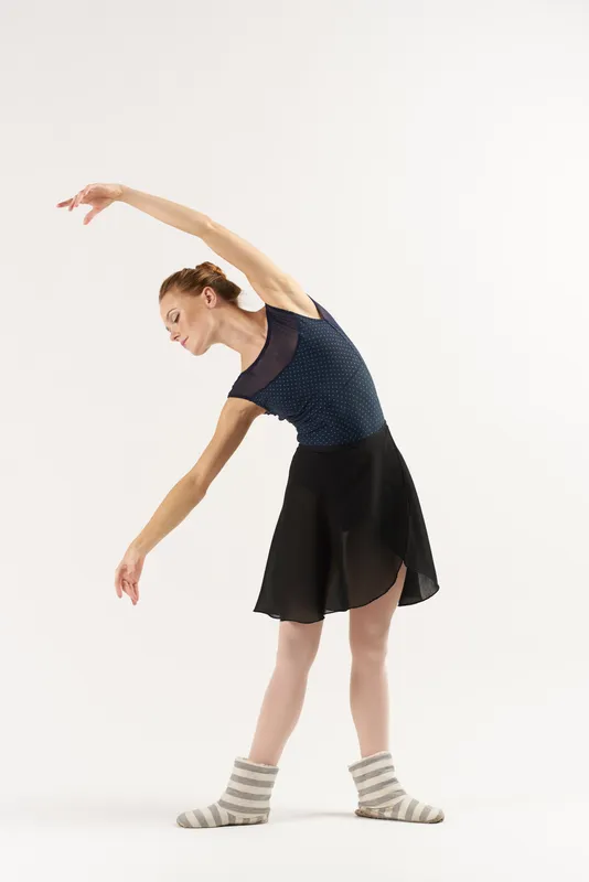 Балерина в пуантах и пачке танцует на светлом фоне в полный рост, выполняя отдельные движения