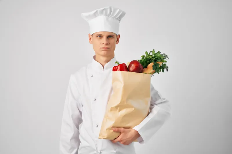 Мужчина в униформе повара занимается упаковкой продуктов для службы доставки еды