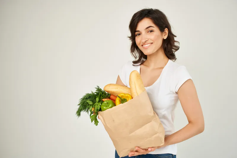 Весёлая брюнетка в белой футболке с пакетом продуктов для доставки из супермаркета