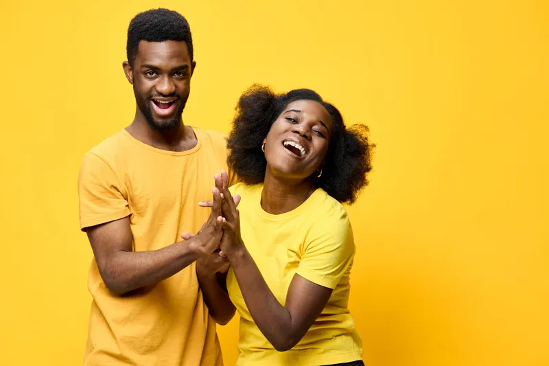 Joyful young couple in matching yellow shirts, celebrating happiness and love against a vibrant yellow backdrop