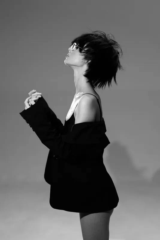 Black and white portrait of a stylish woman with short hair wearing a loose jacket expressing emotion in studio.