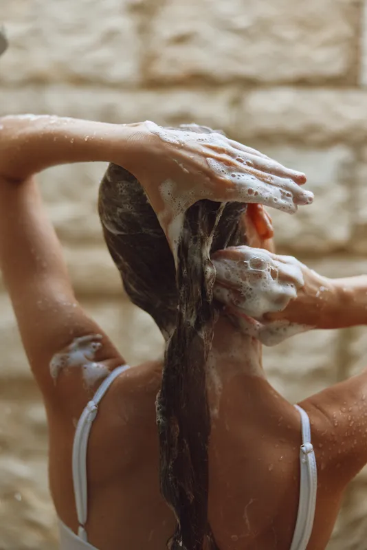 woman washing hair with shampoo, lathered with foam, wet long hair in shower, close-up back view, skincare hygiene routine