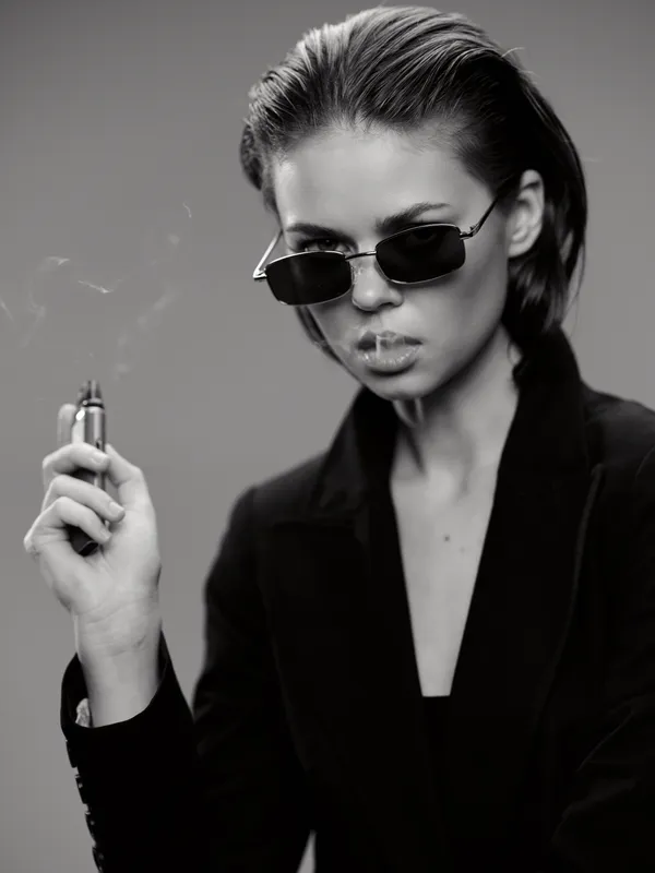 Stylish woman in sunglasses holding a lighter with smoke, black and white portrait, confident expression, modern fashion style.