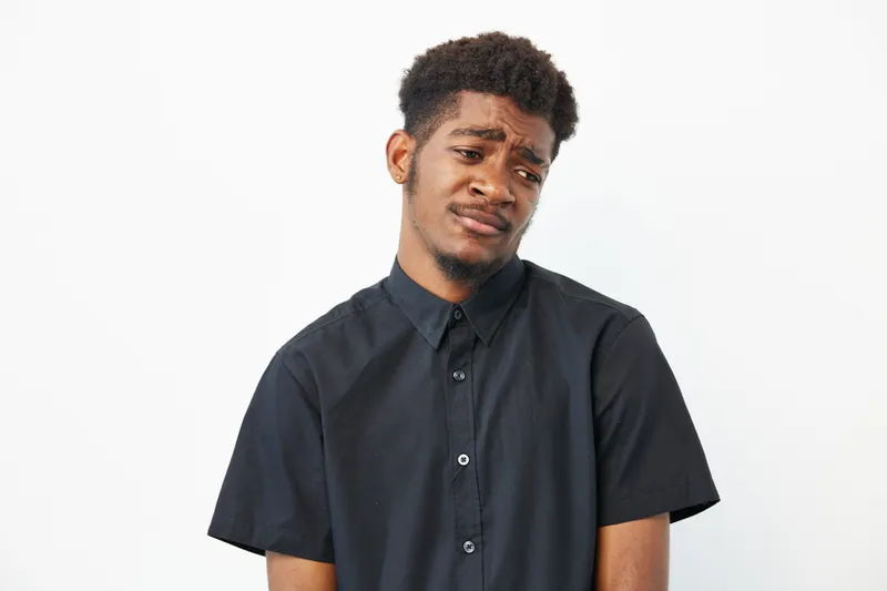 A thoughtful black man shows a mix of emotions while wearing a stylish black shirt. Perfect for concepts of introspection and vulnerability in modern life.