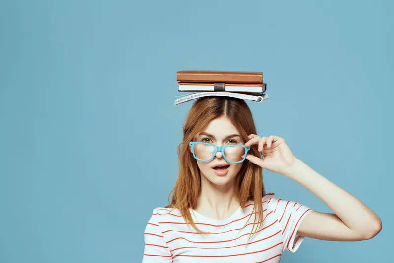 Студентка держит книги на голове на фоне синего цвета, что символизирует научное образование